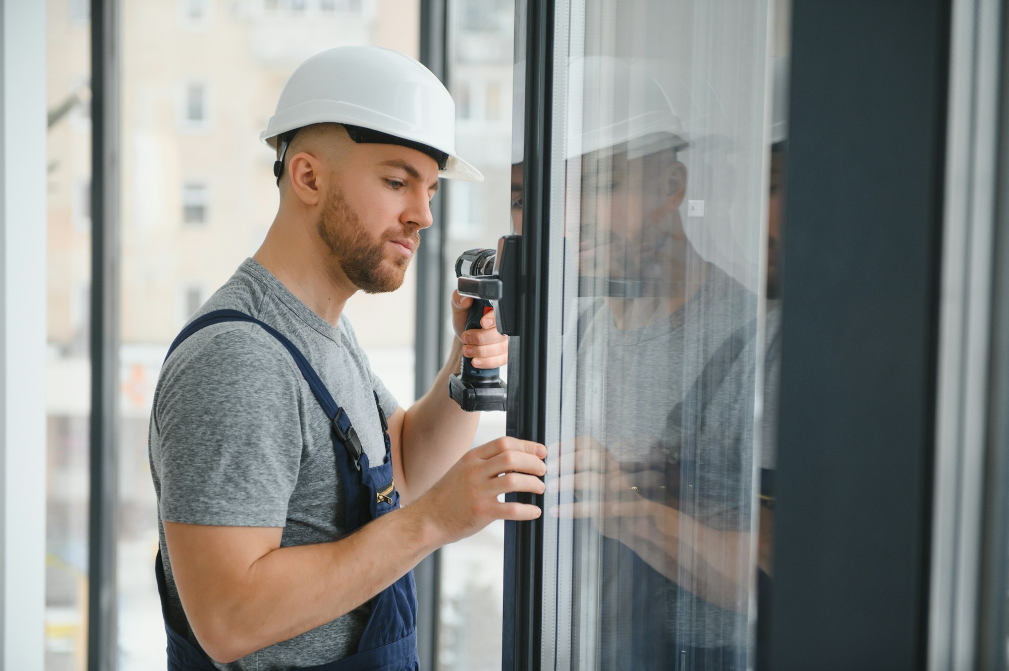 Workman in overalls installing or adjusting plastic windows in the living room at home